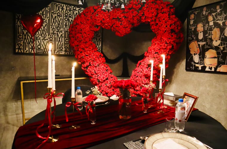 A red rose heart lit by candles above a dressed table