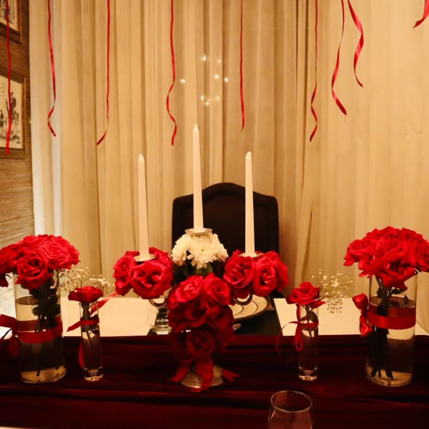 A table dressed with red roses, white tapers and hanging ribbons